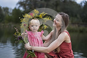 Mom and little daughter are resting by the river. Child in wreath of flowers