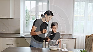 Mom and little daughter sift flour through a sieve into a bowl in the kitchen