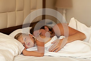 Mom and little daughter sleep hugging on bed. Innocence and hugs