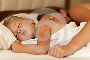 Mom and little daughter sleep hugging on bed. Innocence and hugs