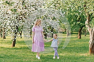 Mom and little daughter are walking through a blooming spring garden