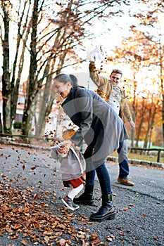 Mom and little girl dodge falling leaves from the bag in the hands of dad