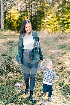 Mom with a little girl walks along the lawn in the forest, holding hands