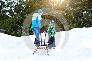 Mom and little son, go with sleds to the hill to ride. Winter fun for family Christmas vacation.