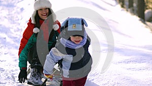 Mom and little son have fun playing in the snow. They ride a sleigh.