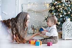 Mom with little son playing with colored blocks near the Christmas tree