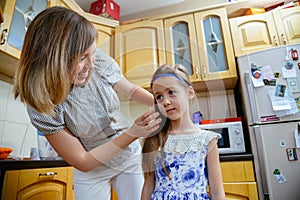 Mom makes daughter hairstyle in the kithen photo