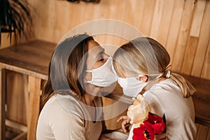 Mom in a mask kisses a little daughter. Blond girl congratulates mom with mother`s day