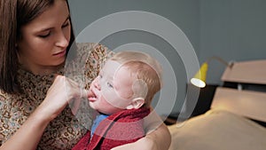 Mom massages baby gums using toothbrush massager worn on finger and gum gel. Teething concept. Slow motion and medium