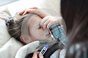 Mom measuring temperature of sick little girl with thermometer