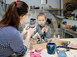 Mom photographs her daughter on a smartphone during a ceramics workshop