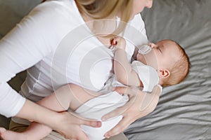 Mom places sleeping newborn baby with pacifier on bed next to her, gently strokes him , hugs him. Safety, care