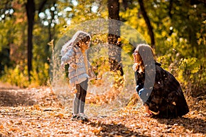 Mom playing with daughter, throw dry yellow fallen leaves. walks in autumn Park