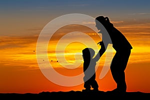 Mom plays with the child on the snow at sunset