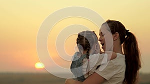 Mom plays with her daughter and shows the child the sunset. Happy family, mom and daughter in the field look at the sun