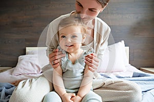 Mom plays with her little daughter in the bedroom. Gentle hugs and fun.