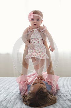 Mom plays with her little daughter on the big bed in the bright bedroom