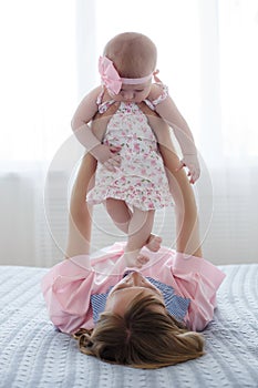 Mom plays with her little daughter on the big bed in the bright bedroom