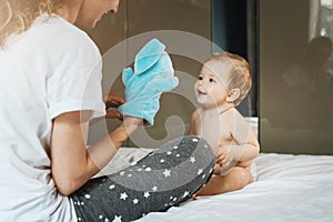 Mom plays with nine-month-old baby girl with soft toy hare. Family leisure. Mom with child play together at home sitting on bed