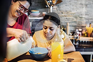 Mom pouring milk to daughter cereal bowl