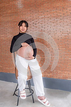 Mom pregnant woman in a dress holds hands on belly on red brick background, Waiting for the birth of your baby with love