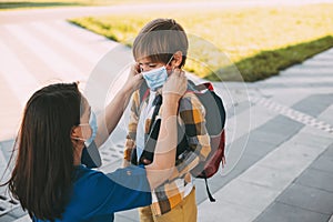 Mom puts a child a mask and escorts to school or kindergarten. A boy with a masked backpack during a coronavirus. Side view