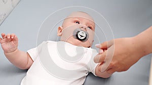 Mom puts newborn to bed in crib, strokes head, holds hand, baby sucks pacifier, close-up. Concept of infancy, childhood