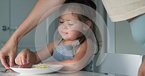 mom puts plate of food on the table in front of the child, girl eat pasta spaghetti, happy preschool child eating fresh