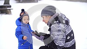 Mom puts on ski gloves and tells something to a little girl crouching in the snow