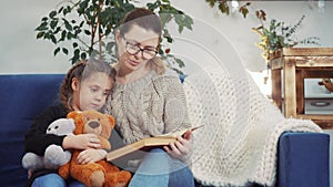 Mom read a book to her daughter at home. Kid dream coronavirus stay home concept. Mom is sitting on the couch with her