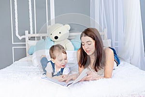 Mom reads a book to the child or teaches him at home on the bed Happy loving family. Mom and son