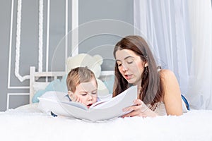 Mom reads a book to the child or teaches him at home on the bed Happy loving family. Mom and son