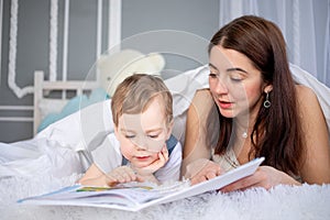 Mom reads a book to the child or teaches him at home on the bed Happy loving family. Mom and son