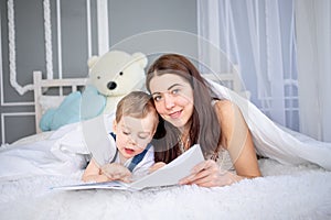 Mom reads a book to the child or teaches him at home on the bed Happy loving family. Mom and son