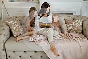 Mom reads a book to the children. A woman tells a story to a boy and a girl before going to bed. Mom daughter and son relax