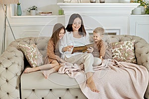 Mom reads a book to the children. A woman tells a story to a boy and a girl before going to bed. Mom daughter and son relax at