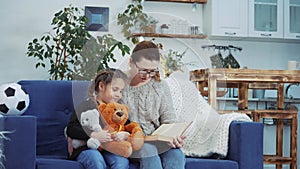 mom reads a book to her daughter at home. kid dream coronavirus stay home concept. mom is sitting on the couch with her