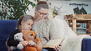 Mom reads a book to her daughter at home. Kid dream coronavirus stay home concept. Mom is sitting on the couch with her