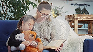 mom reads a book to her daughter at home. kid dream coronavirus stay home concept. mom is sitting on the couch with her
