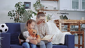 mom reads a book to her daughter at home. kid dream coronavirus stay home concept. mom is sitting on the couch with her