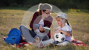 mom reads a book to her daughter in the park on lifestyle vacation. happy family kid dream concept. mother reads a book