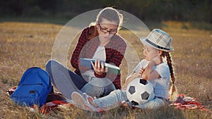 mom reads a book to her daughter in the park lifestyle on vacation. happy family kid dream concept. mother reads a book