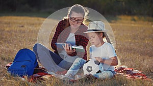 Mom reads a book to her daughter in the park on vacation. Happy family kid dream concept. Lifestyle mother reads a book