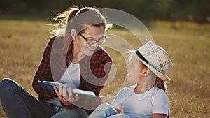 mom reads a book to her daughter in the park on vacation. happy family kid dream concept. mother reads a book to his