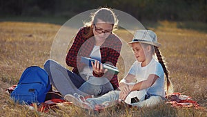 mom reads a book to her daughter in the park on vacation. happy family kid dream concept. mother reads a book to his