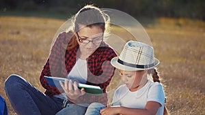 mom reads a book to her daughter in the park on vacation. happy family kid dream concept. mother reads a book to his