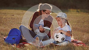 mom reads a book to her daughter in the park on vacation lifestyle. happy family kid dream concept. mother reads a book