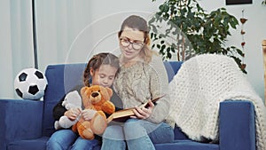 mom reads a book to lockdown her daughter at home. kid dream coronavirus stay home concept. mom is sitting on the couch