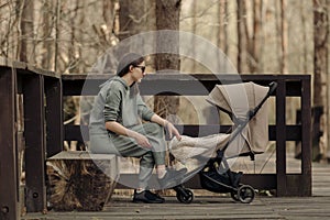 The mom is relaxing on the bench while her child is sleeping in the stroller