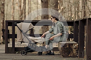 The mom is relaxing on the bench while her child is sleeping in the stroller